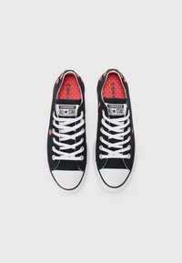 Baskets en toile noire avec bout en caoutchouc blanc, dotées de lacets blancs, d'une doublure rouge à motif et de petits accents en forme de fraise sur les côtés.