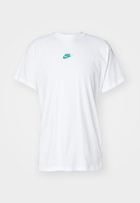 Camiseta de algodón blanca con un logo verde de Nike en el pecho. Ajuste estándar con mangas cortas y un escote redondo.