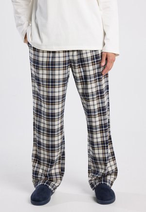 Loungebroek met ruitpatroon in beige, marineblauw en bruin, gemaakt van zachte stof. Losse pasvorm met wijde pijpen, gecombineerd met marineblauwe slippers.