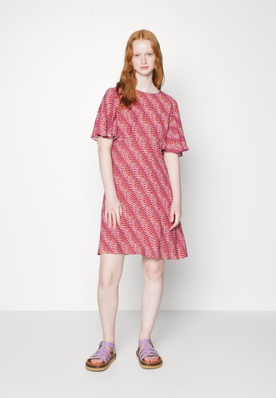 Vestido de mangas curtas, até ao joelho, em tecido com padrão rosa e vermelho; combinado com sandálias lavanda com várias tiras e sola espessa.
