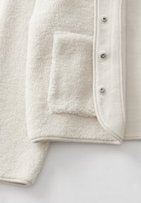 Giacca in pile color crema con superficie morbida e testurizzata, tasca laterale e bottoni a pressione argentati lungo l'apertura frontale.