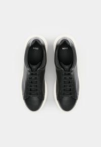 Černé kožené tenisky s hladkou texturou, bílou gumovou podrážkou a kulatou špičkou. Na jazyku je diskrétní značení.