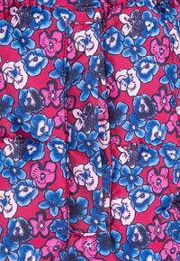 Klart rosa tyg med tät tryck av blå, vita och lila blommor som omger en vertikalt sydd ficka med ett lock.