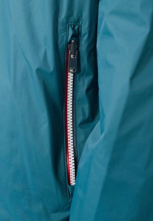 Chaqueta impermeable azul con cremallera en el lado izquierdo, detalles en rojo y acabado texturizado. La cremallera tiene una lengüeta negra para facilitar su apertura.