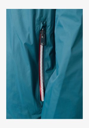 Blauwe waterdichte jas met een rits aan de linkerkant met rode accenten en een gestructureerde afwerking. De rits heeft een zwart trekkoord voor gemakkelijk openen.