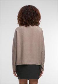 Bézs színű kötött pulóver laza szabással, leejtett vállakkal és egyenes szegéllyel, fekete szoknyával párosítva. Simogató textúra, minimalista design.