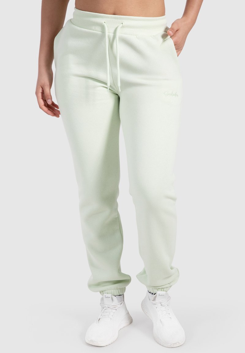 Ljusgröna, bomullsblandning sweatpants med elastisk midja, snörning, fickor och elastiska muddar, i kombination med vita sneakers.