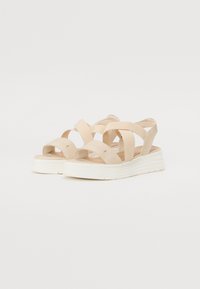 Sandales à talons compensés beige avec des lanières croisées, fabriquées en matériau lisse. Elles présentent une semelle blanche texturée et un design à dos ouvert.