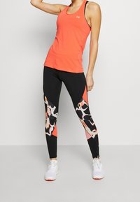 Korálový sportovní top s návrhem racerback, doplněný černými legínami s barevným abstraktním vzorem a přiléhavými ke kotníkům.