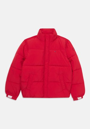 Giacca a vento rossa con colletto alto, tasche laterali e polsini elastici. Presenta un motivo a righe orizzontali e un'etichetta con logo sul petto.