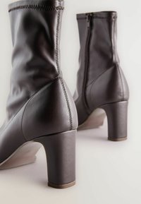 Stivaletti in pelle marrone con una texture liscia, robusti tacchi a blocco, cerniere laterali e dettagli di cucitura a contrasto.