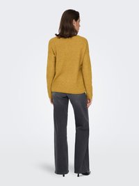 Senfgelber Rippstrickpullover mit lässiger Passform, kombiniert mit hoch taillierten, dunkelgrauen Jeans mit geradem Bein. Glatte Textur, dezent strukturiert.