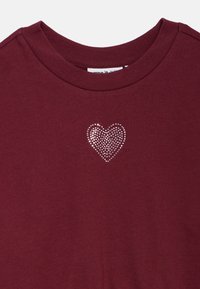 Camiseta de algodão bordô com decote redondo, apresentando um design de coração em strass prateado no lado esquerdo do peito. Textura suave.