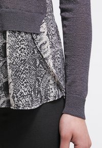 Haut à manches longues en tricot gris foncé texturé, superposé à un tissu à imprimé serpent crème et noir au niveau de l'ourlet.