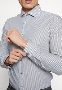 Striped button-up shirt in navy and white, featuring a spread collar, long sleeves with button cuffs, and a fitted design.