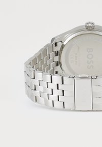 Montre en acier inoxydable argenté avec un bracelet en maille, boîtier rond et finition polie. Elle dispose d'un fermoir de marque et d'un fond résistant à l'eau.