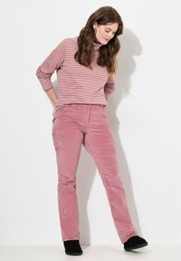 Rosa kordflorsebyxor med rak bendesign, kombinerat med en rosa och vit randig turtlenecktröja. Svart fotbeklädnad bärs.