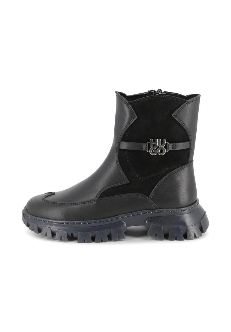 Botines negros de cuero liso y ante con suela de goma robusta, que cuentan con una correa decorativa con el logo en el lateral.