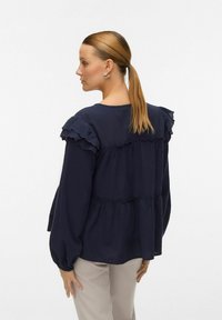 Blusa blu navy con spalle arruffate, design a peplum e cuciture arricciate. Maniche lunghe con polsini elasticizzati, realizzata in tessuto leggero.