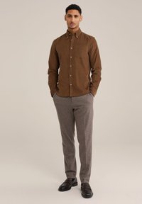 Camisa de botones de pana marrón con un bolsillo en el pecho, combinada con pantalones grises y zapatos negros. Diseño sencillo y ajuste regular.