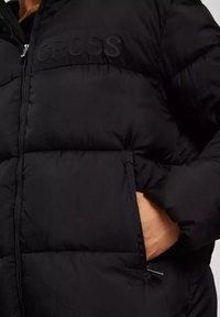 Czarna kurtka puchowa o pikowanym wzorze, z zapięciem na zamek i bocznymi kieszeniami. Nazwa marki "CROSS" wytłoczona na klatce piersiowej. Miękka tekstura.