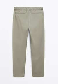 Vista posteriore di pantaloni verde oliva chiaro con una cintura elastica e due tasche a fessura orizzontali vicino alla parte superiore.