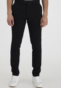 Schwarze Hose mit einem eleganten Design, aus einem glatten Stoff gefertigt. Figurbetonte Form mit einem Knopfverschluss, kombiniert mit weißen Sneakers.