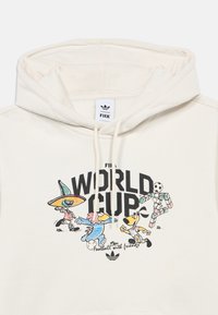Hoodie crème avec un graphique de la Coupe du Monde de la FIFA mettant en scène des personnages de dessin animé colorés, du texte noir et un logo Adidas. Matière en coton doux.