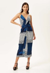 Sleeveless maxi dress featuring a mix of blue, white, and black patterns, including animal prints and geometric shapes, with a cinched front.