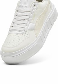 Vita sneakers med en slät läderöverdel, perforerad tå och texturerad vit gummisula. Har framträdande branding och snörningsdesign.