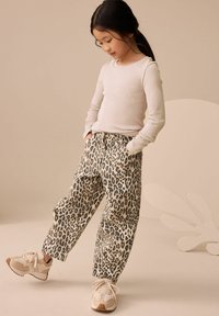 Beżowa bluzka z długim rękawem w połączeniu z luźnymi spodniami w leopardzi wzór. Obuwie to beżowe sneakersy z teksturowaną podeszwą i jasnymi sznurowadłami.