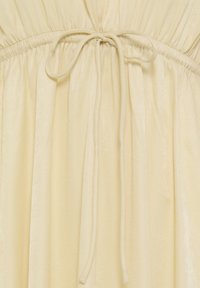 Robe en tissu ivoire froncé avec un fin cordon noué en nœud papillon à la taille, créant de doux plis en dessous.