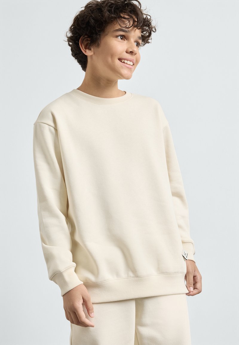 Ljusbeige sweatshirt i mjukt tyg, med rund halsringning, sänkta axlar och ribbade ärmslut och nederkant. Enkel design.