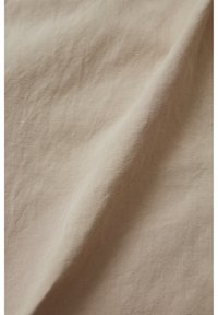 Tessuto di lino con una superficie liscia e leggermente strutturata di un colore beige chiaro, che presenta morbide pieghe e una sottile lucentezza.
