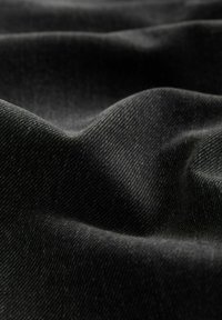 Zwarte denimstof met een textuur en een licht gekreukt oppervlak, met een strakke weving en subtiele variaties in tint.