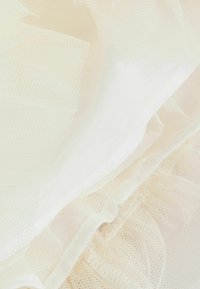 Tessuto di tulle bianco con una consistenza morbida, caratterizzato da strati di volant e una delicata lucentezza. Il materiale ha un aspetto leggero e arioso.