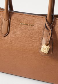 Borsa in pelle marrone con texture a ciottoli, dotata di due manici, hardware color oro e un distintivo charm MK ben visibile attaccato a un lato della borsa.