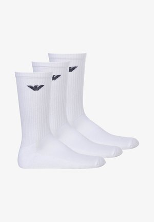 Chaussettes en coton blanches, texture côtelée, longueur mi-mollet, avec un petit logo noir sur le côté. Vendu par lot de trois.