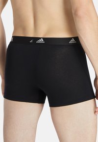 Bóxers ajustados para hombre en color negro. Cuentan con una cintura elástica negra con detalles del logo de Adidas en plata. Material liso y ligeramente brillante.