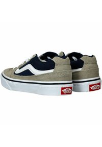 Zapatillas de ante y malla en beige y azul marino con rayas blancas, cierre de cordones y logo rojo en el talón. Suela de goma blanca con ribete negro.