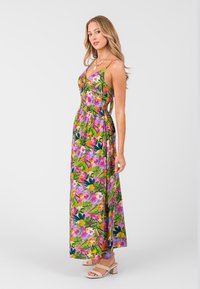 Květinové maxi šaty s růžovým podkladem, zelenými listy a vícebarevnými květinami. Mají tenká ramínka a přiléhavý pas s volným sukní.
