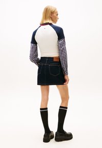 Valge ja tumesinine raglaan-topp, ruudulised pikad varrukad, tume teksaseelik, mustad põlvikud, platvormkingad, seelikul nähtav silt.