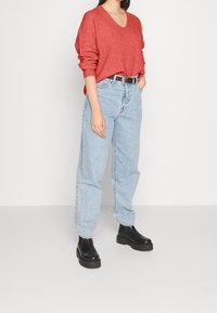 Röd stickad tröja med V-ringning, avslappnad passform, i kombination med ljusblå höga jeans och svarta plattformstövlar. En enkel bälte accentuerar outfiten.