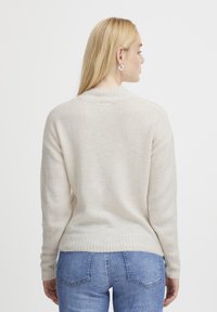 Maglione morbido in maglia di un beige chiaro con orlo e polsini a coste, caratterizzato da un collo a giro e spalle scese. Visualizzazione dal retro.