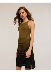Pletené šaty s cik-cak vzorem, přecházející od olivové barvy na vrchu k černé na lemu. Bezrukávový design s kulatým výstřihem.