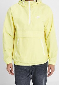 Gul Nike halvdraget jacka med halvdragkedja fram, två dragkedjefickor, elastiska fållar och kortad nederkant. Lättviktigt, vattenavvisande material.