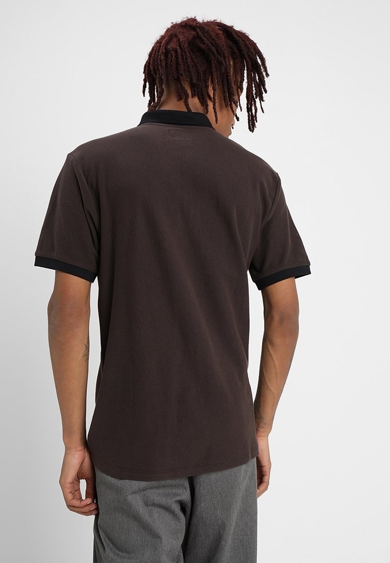 Polo marron à manches courtes avec un col et des poignets noirs, présentant une texture douce et une coupe droite, vu de dos.