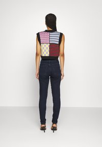 Top sin mangas de punto con diseño de patchwork multicolor en rosa, morado y negro. Los patrones texturizados incluyen cuadros, zigzags y olas.