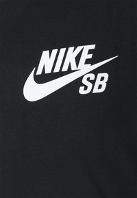 Fekete szövet póló, amelyen egy kiemelkedő fehér Nike SB logó található. Az anyag sima kinézetű, enyhén texturált felülettel.