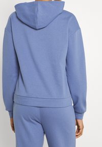 Sweatshirt i mjukt, ljusblått tyg med huva, sänkta axlar och ribbade manschetter och nederkant. Bakifrån visar den en slät textur.